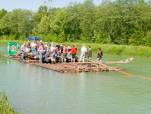 Gruppe auf dem Holzfloss f&auml;hrt gem&uuml;tlich auf der Isar durch gr&uuml;ne Auen
