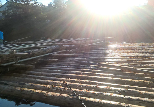 Flöße aus Baumstämmen liegen bereit im Sonnenlicht an der Ablegestelle